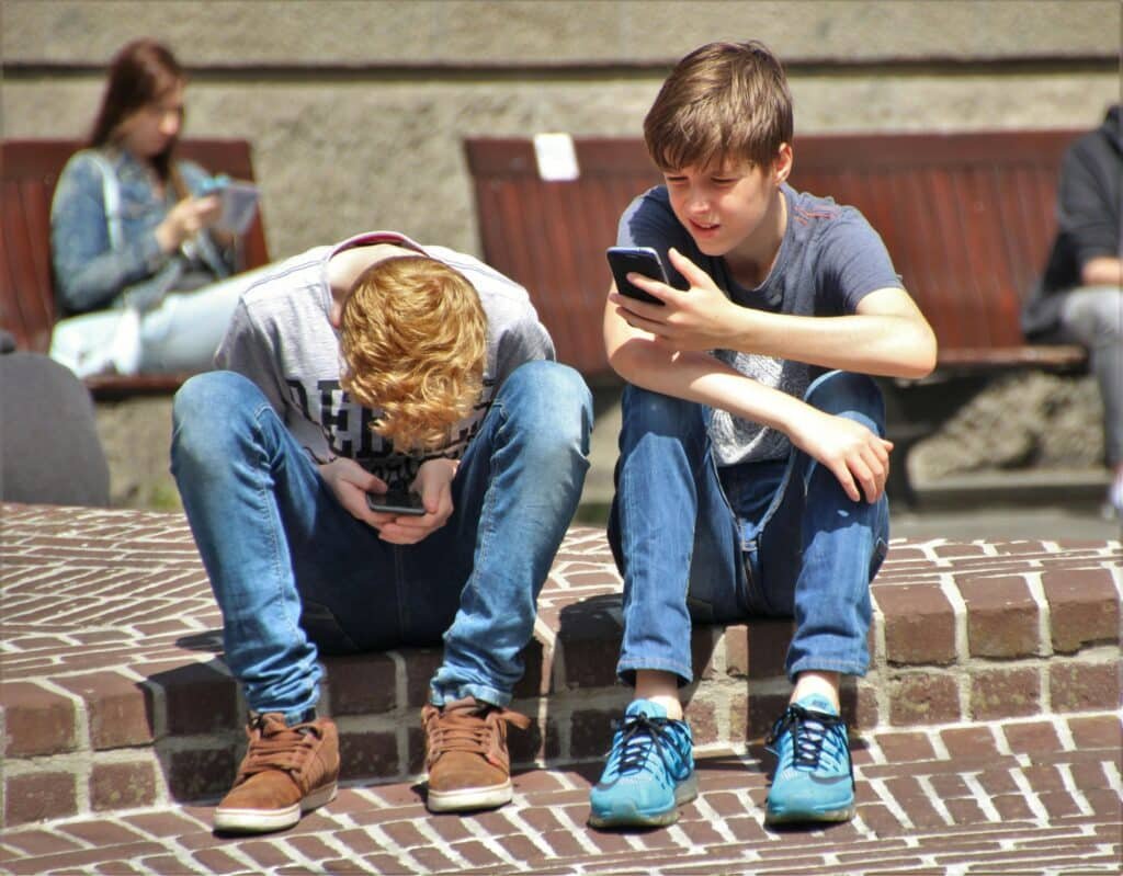 2 children sitting in their phones outside